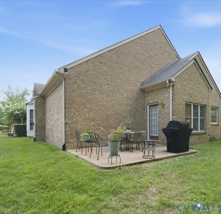 Brick exterior with a gabled roofline, concrete patio, wooded rear view.