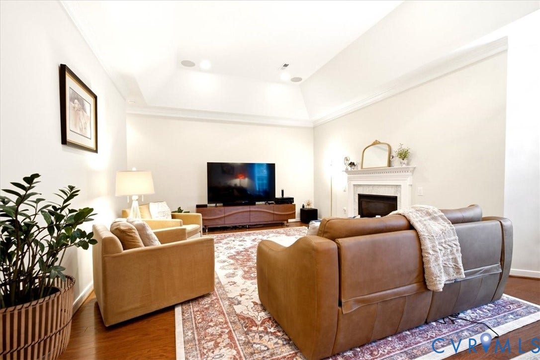 Vaulted ceiling with recessed lighting, crown molding, a decorative fireplace, and wood-finish flooring