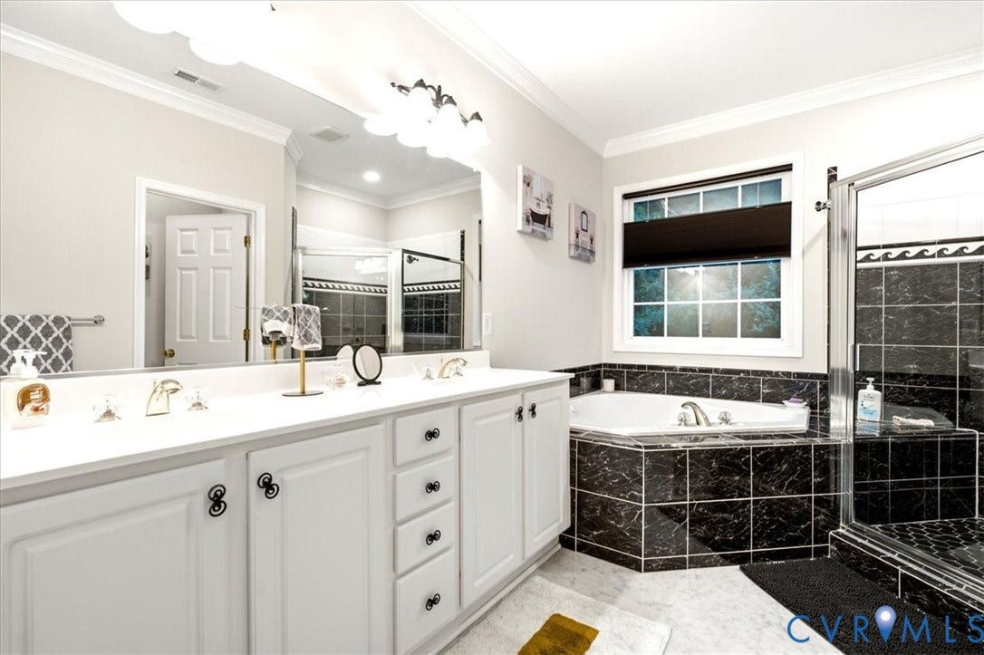 Dual vanity with white cabinetry, built-in corner soaking tub, separate glass-enclosed shower, and dark marble-look tile accents