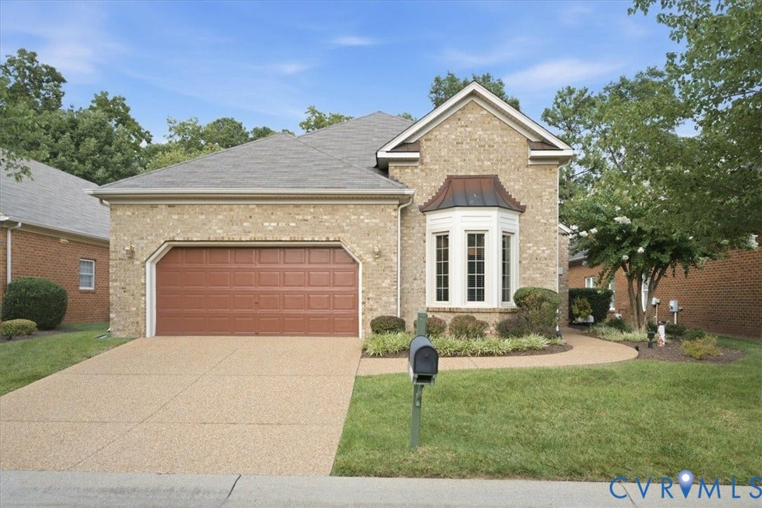 Brick exterior with a peaked roofline, a bay window with a copper-tone awning, and an attached two-car garage