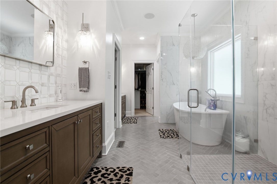 435 Shadow Creek Lane, Manakin Sabot, VA 23103 Spacious bathroom featuring a glass-enclosed shower, freestanding soaking tub, wood-finish vanity with a white countertop, and tiled walls with a herringbone-patterned floor