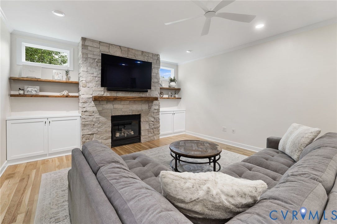 12305 Bradford Landing Way, Wyndham, Glen Allen, VA 23059 Living area featuring a stacked stone fireplace with a wood-finish mantle, built-in cabinetry, floating wood-finish shelving, and light wood-finish flooring