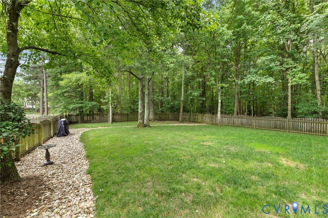 12305 Bradford Landing Way, Wyndham, Glen Allen, VA 23059 Expansive fenced backyard featuring a manicured lawn, mature trees, a gravel pathway, and a privacy fence
