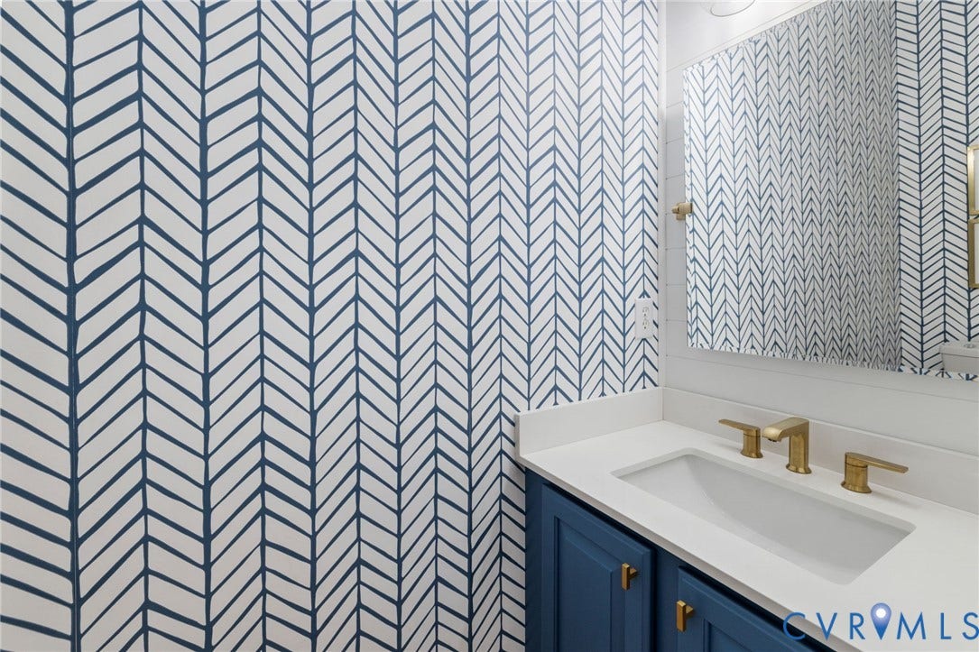 12305 Bradford Landing Way, Wyndham, Glen Allen, VA 23059 renovated 1/2 bath on first floor featuring a blue and white patterned wall covering, a white countertop, a built-in rectangular sink with a gold-finish faucet, and a blue vanity with gold-finish hardware