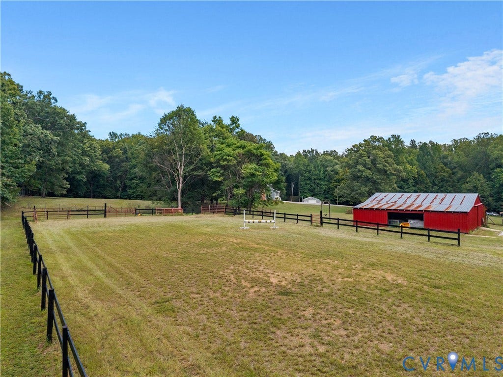 3927 Hughes Creek Road, Powhatan, VA 23139 Expansive grassy acreage featuring perimeter fencing, a red barn with a metal roof, and distant mature trees