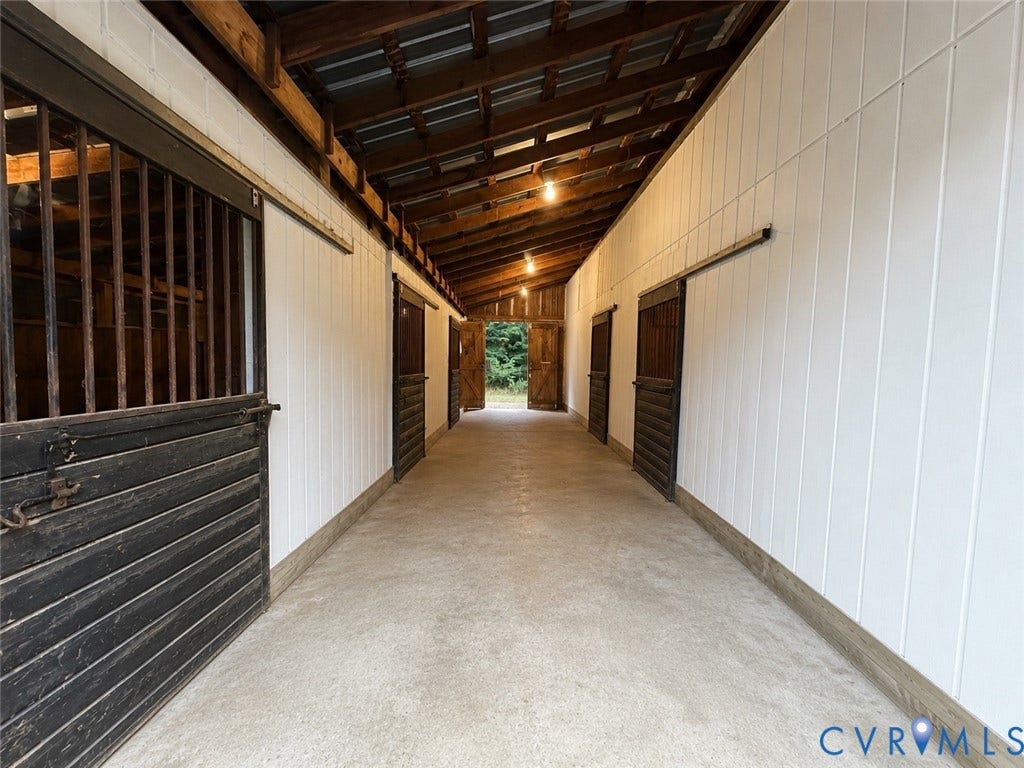 3927 Hughes Creek Road, Powhatan, VA 23139 Covered stable aisle featuring multiple stalls with sliding wood doors, exposed wood beam ceiling, and concrete flooring
