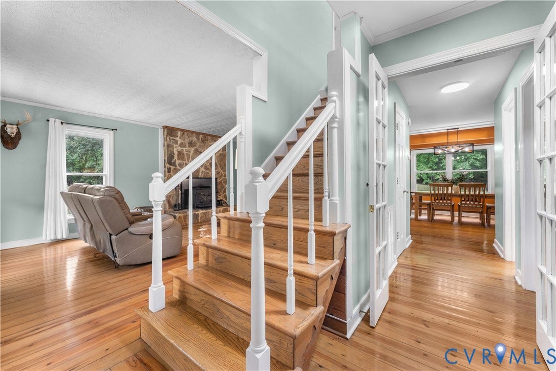 3927 Hughes Creek Road, Powhatan, VA 23139 Hardwood flooring throughout, a staircase with white balusters, a stone-clad fireplace, and white French doors