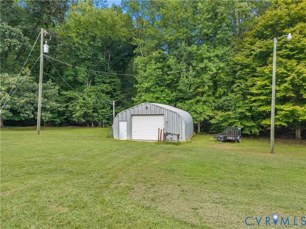 3927 Hughes Creek Road, Powhatan, VA 23139 Expansive grassy area with a freestanding metal storage structure featuring a roll-up garage door and a separate entry door