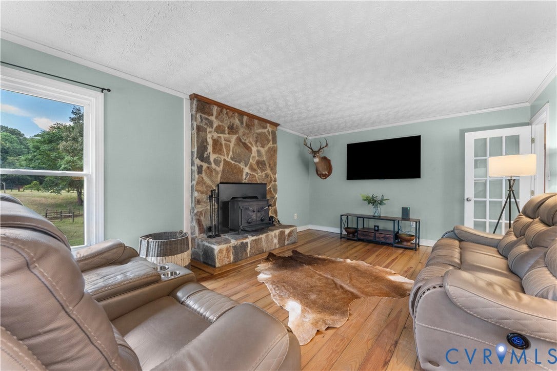 3927 Hughes Creek Road, Powhatan, VA 23139 Stone-clad fireplace with a black wood-burning stove, wood-finish flooring, and a white interior door with glass panels