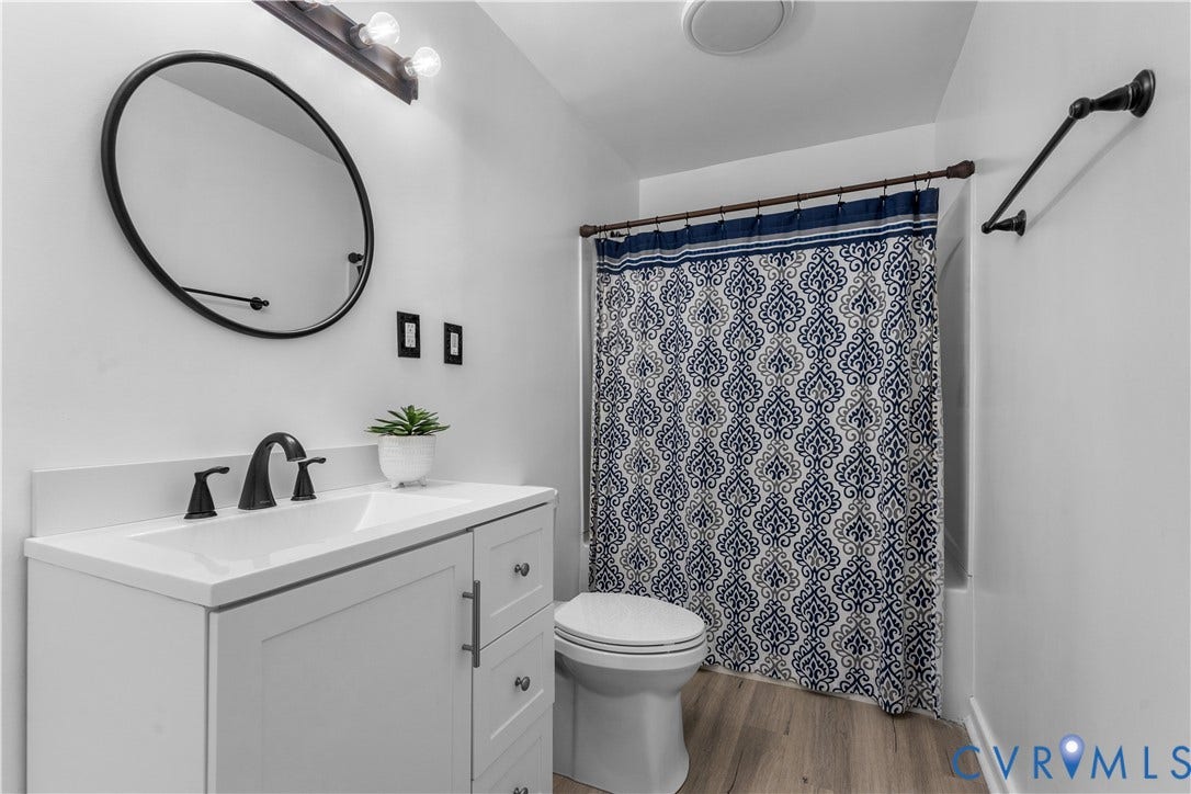 3927 Hughes Creek Road, Powhatan, VA 23139 White vanity with integrated sink, matte black faucet, round wall-mounted mirror, and wood-finish flooring