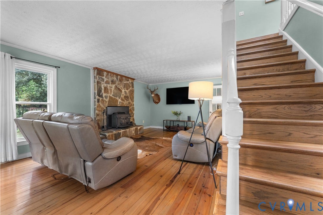 3927 Hughes Creek Road, Powhatan, VA 23139 Wood-finish flooring, stone fireplace with a wood-burning insert, and wood stairs with a white balustrade
