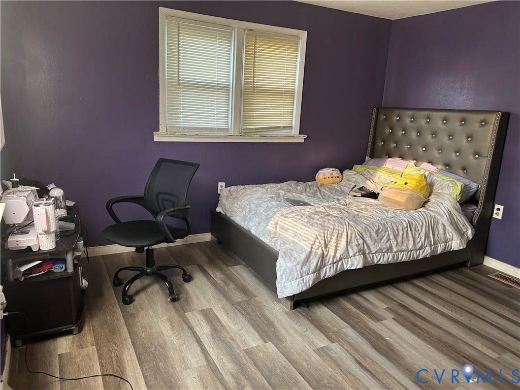 Room featuring wood-finish flooring, a window with blinds, and a neutral-toned baseboard