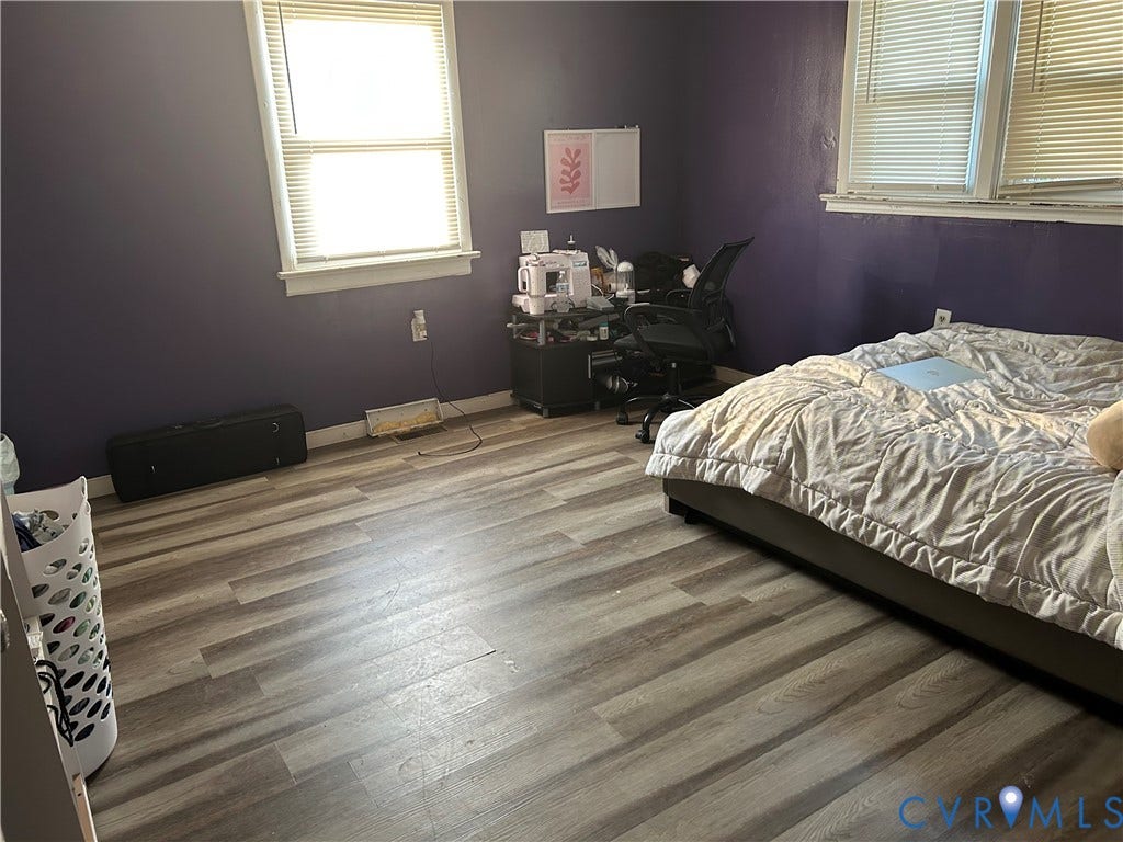 Room featuring wood-finish flooring, two windows with white blinds, and a built-in wall outlet