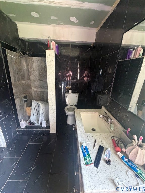 Bathroom featuring black-veined wall tiling, coordinating floor tiles, a shower enclosure with gray-toned tile, a single vanity with an integrated sink, and a speckled countertop
