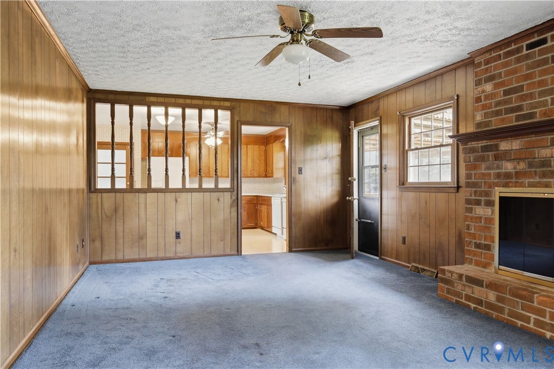 3641 Kiefer Road, Bermuda, Chester, VA 23831 Living area featuring extensive wood paneling, a brick fireplace with hearth, blue carpeting, a ceiling fan, and a window providing natural light
