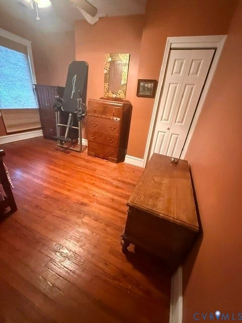 Hardwood flooring throughout featuring a ceiling fan, window with blinds, and a closet with bifold doors