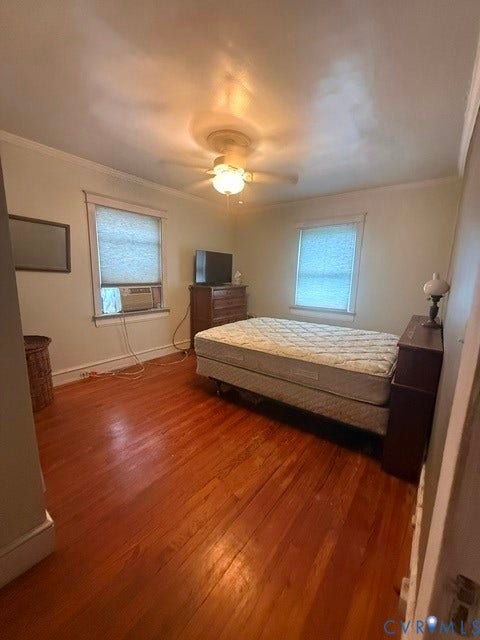 Room featuring wood flooring, two windows with blinds, a ceiling fan with integrated lighting, and crown molding