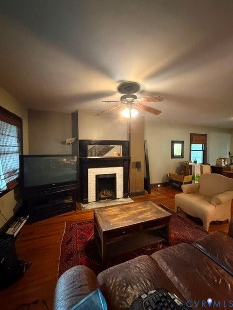 Fireplace with decorative white tile surround, wood-finish flooring, and ceiling fan