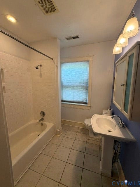 Tiled flooring, pedestal sink, wall-mounted medicine cabinet, wall-mounted light fixture, and a tub with a shower head