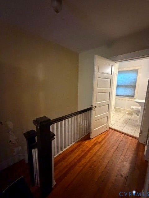 Hardwood flooring throughout, with a paneled interior door opening to a bathroom featuring tiled flooring, a window, and a toilet