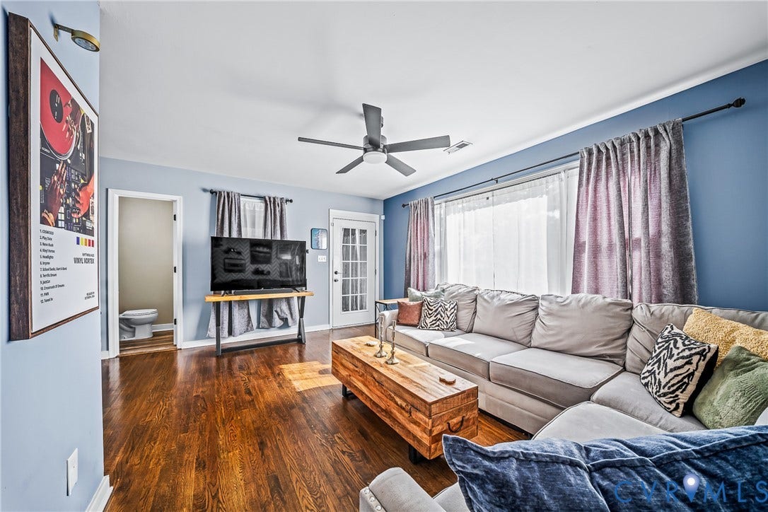 3304 Carlton Road, Henrico, VA 23223 Living area featuring rich wood flooring, light blue walls, and a large window with sheer and blackout curtains