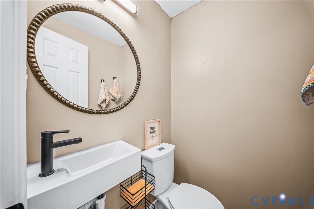 3304 Carlton Road, Henrico, VA 23223 Half Bathroom featuring a wall-mounted rectangular basin, a matte black single-handle faucet, and a large oval mirror with a textured frame