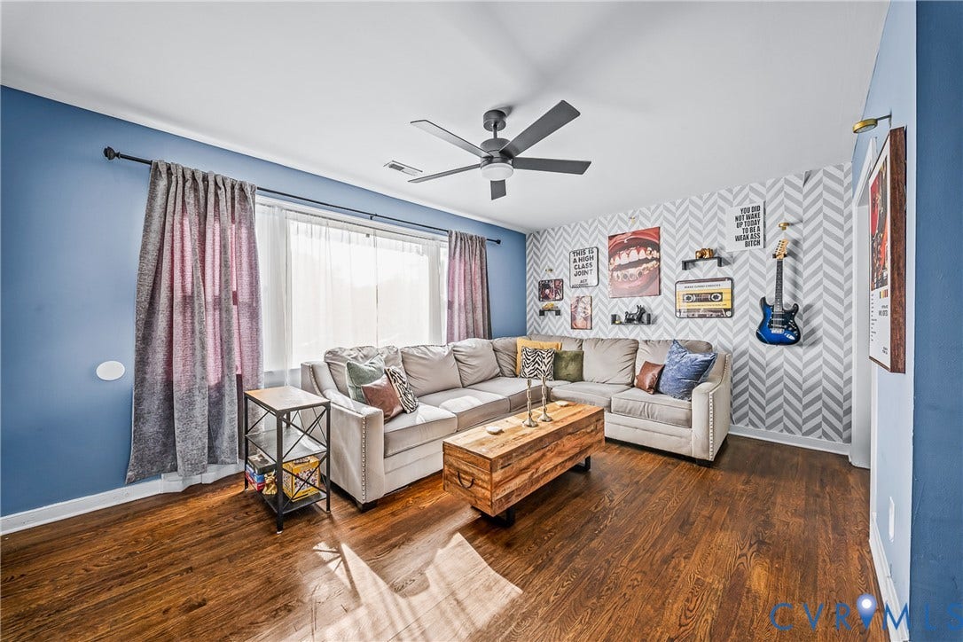 3304 Carlton Road, Henrico, VA 23223 Spacious living area featuring wood flooring, a contemporary ceiling fan, and a prominent accent wall with a geometric pattern