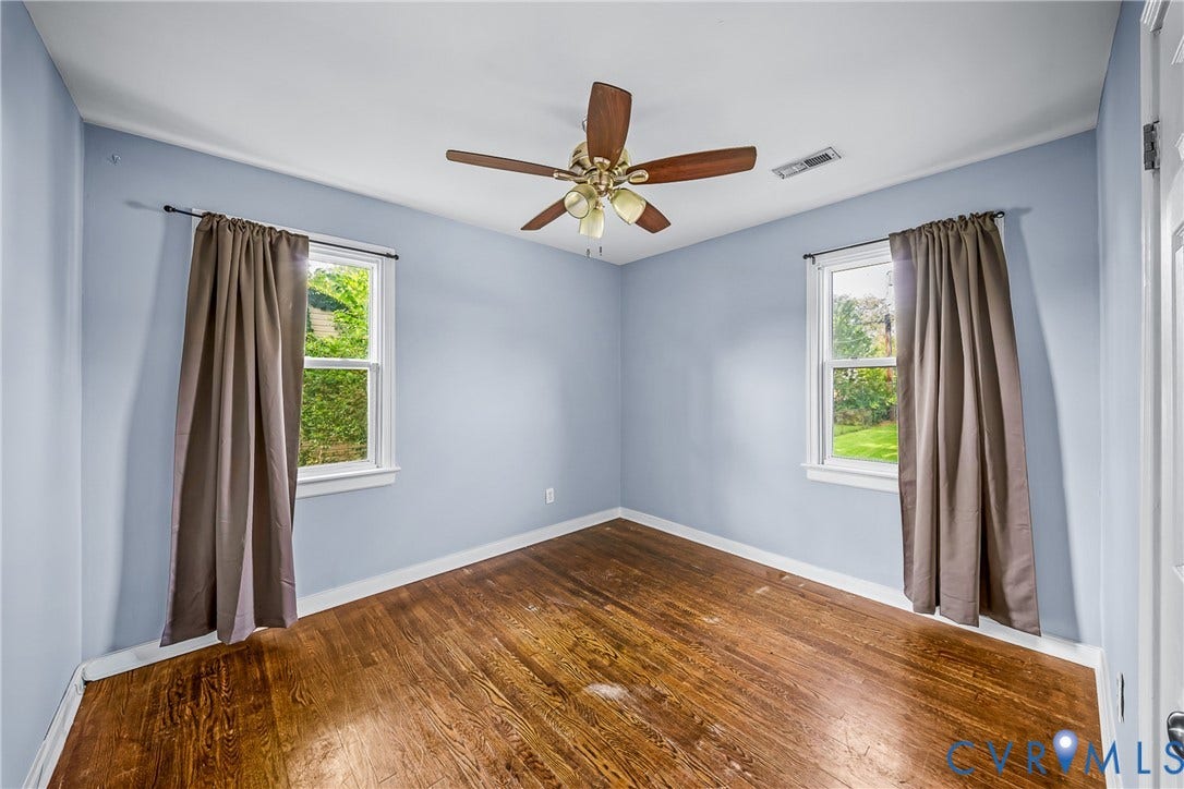 3304 Carlton Road, Henrico, VA 23223 #2 Hardwood flooring throughout this room featuring two windows with white trim, a ceiling fan, and light blue walls