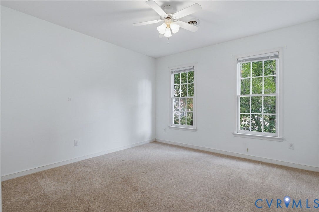 Carpeted room featuring two double-hung windows, a ceiling fan, and white baseboards