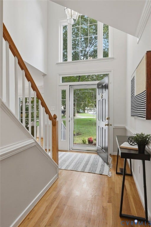 Two-story foyer featuring hardwood flooring, a white spindle staircase with wood handrail, an exterior door with sidelights, and a transom window