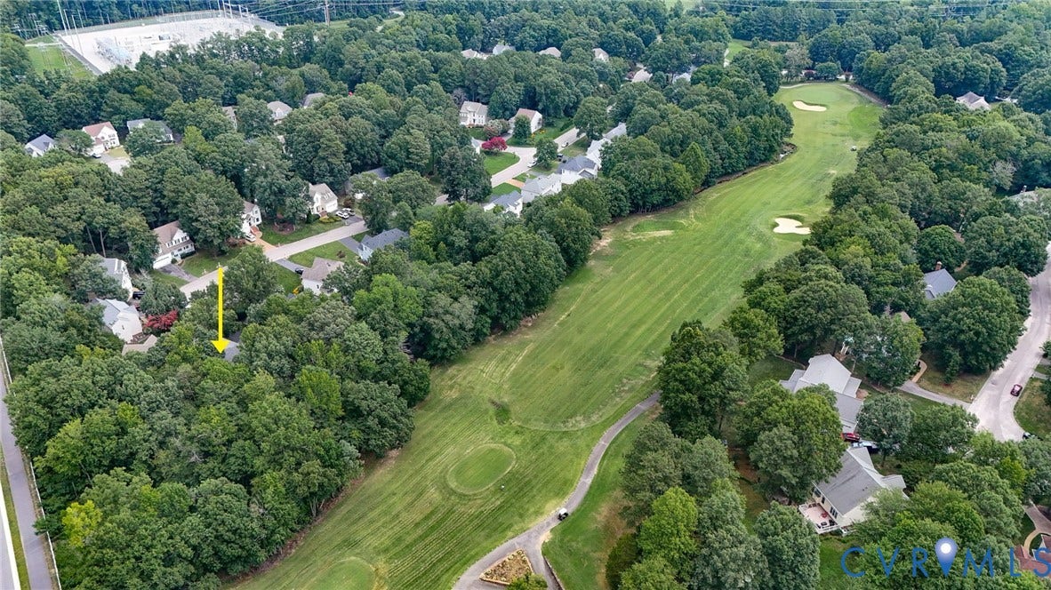 Aerial view showcasing a residential area enveloped by mature trees, with a manicured golf course bordering the properties