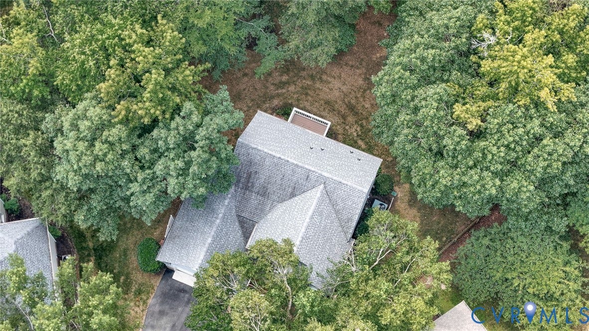Residence with a multi-pitched shingle roof surrounded by mature trees