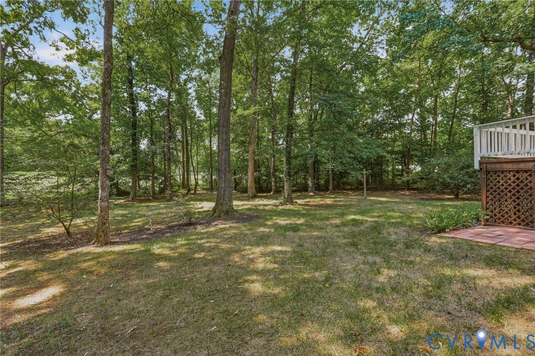 Expansive backyard featuring a lush lawn, mature trees, and a ground-level brick patio