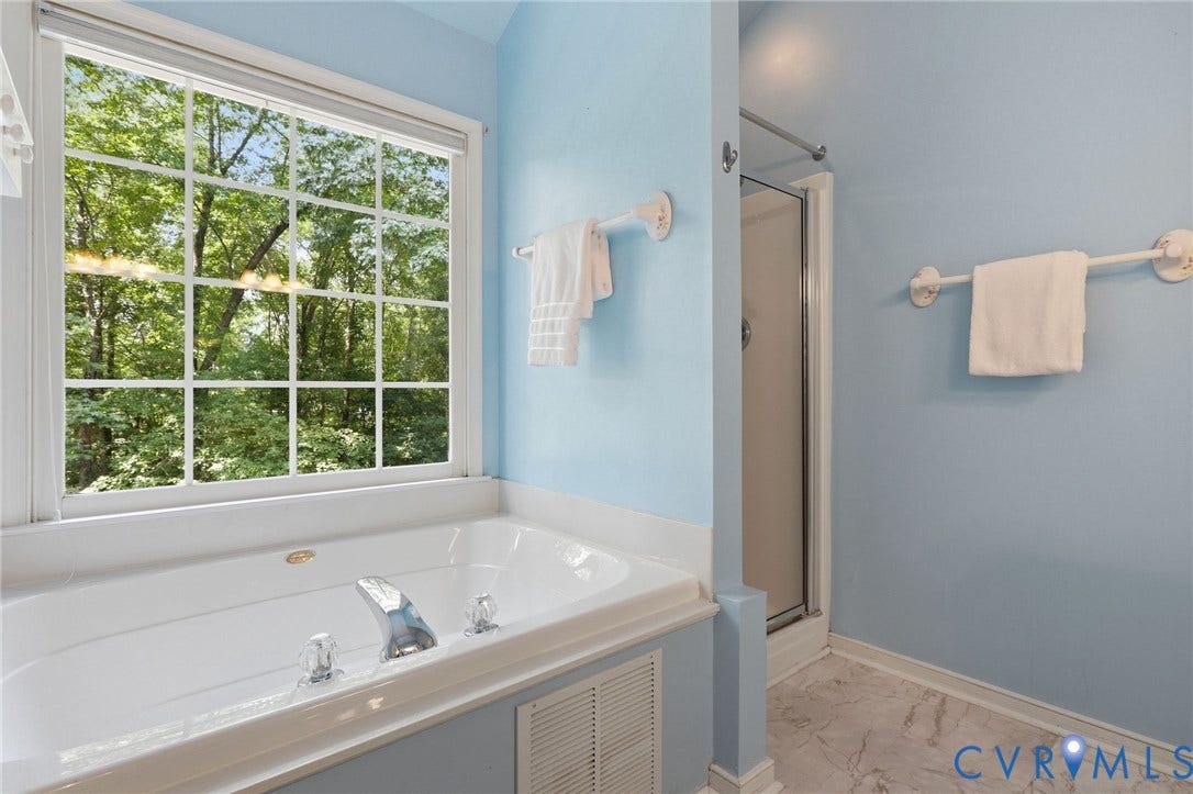 Soaking tub with chrome fixtures, large window with grid panes, glass-enclosed shower, and light blue wall finish