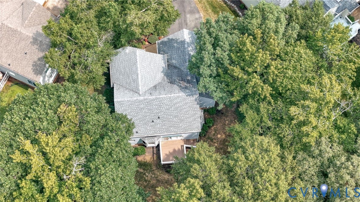 Aerial view of the property showcasing a multi-level home with a gray shingle roof, surrounded by mature trees