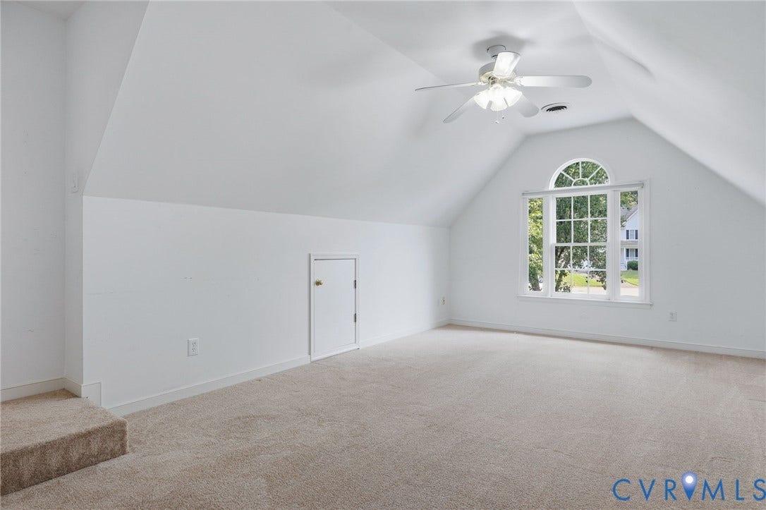 Spacious bonus room featuring carpeted flooring, sloped ceilings, and a large arched window