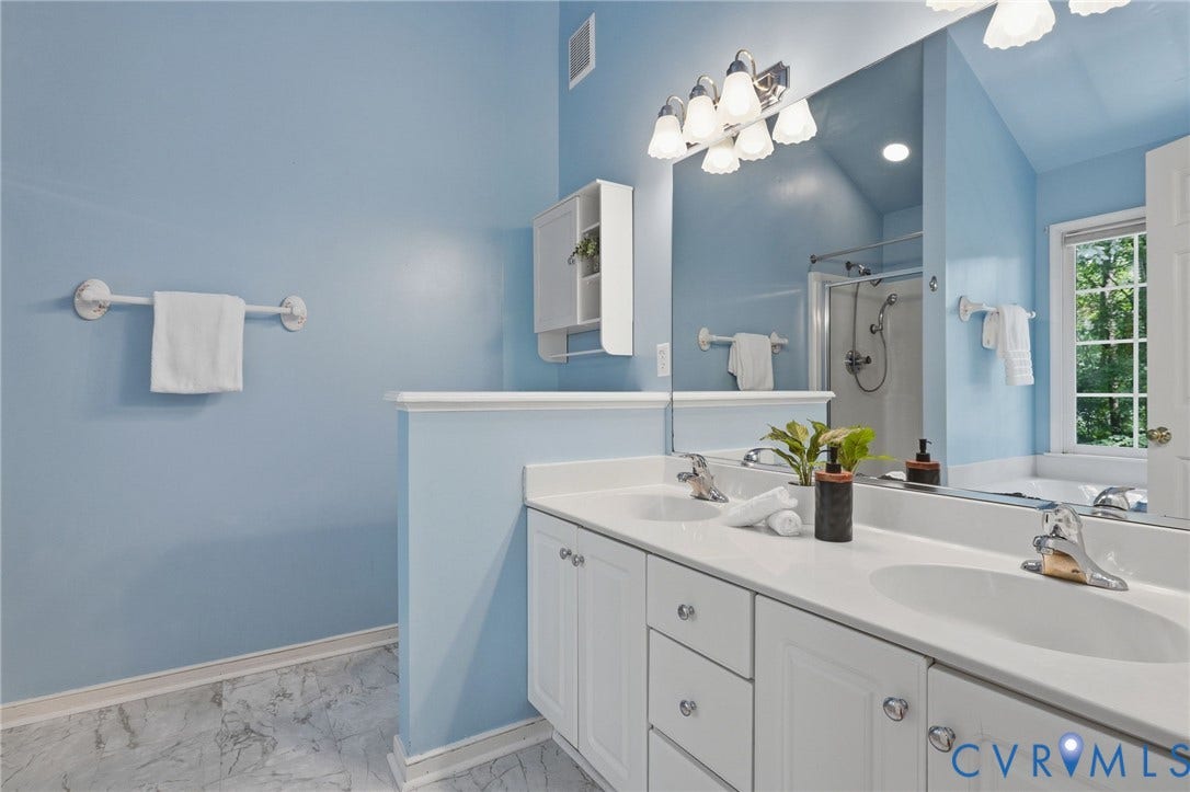 Dual vanity with white cabinetry and integrated sinks, complemented by a large wall-mounted mirror and a multi-bulb light fixture