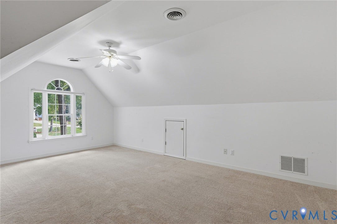Spacious room featuring vaulted ceilings, a prominent arched window, and neutral carpet flooring