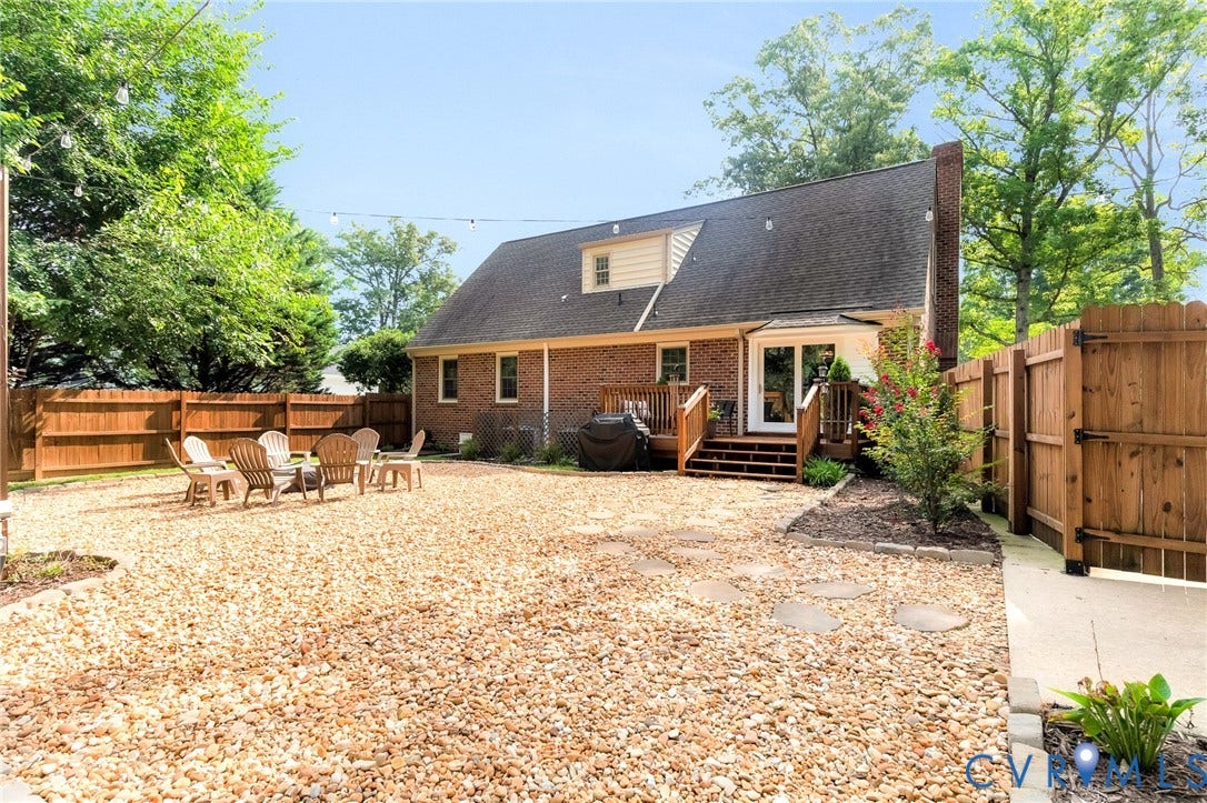 8800 Shewsbury Drive, New Kent, VA 23124 Expansive gravel backyard featuring a privacy fence, a multi-level wood deck, double glass doors, a dormer window, and mature trees