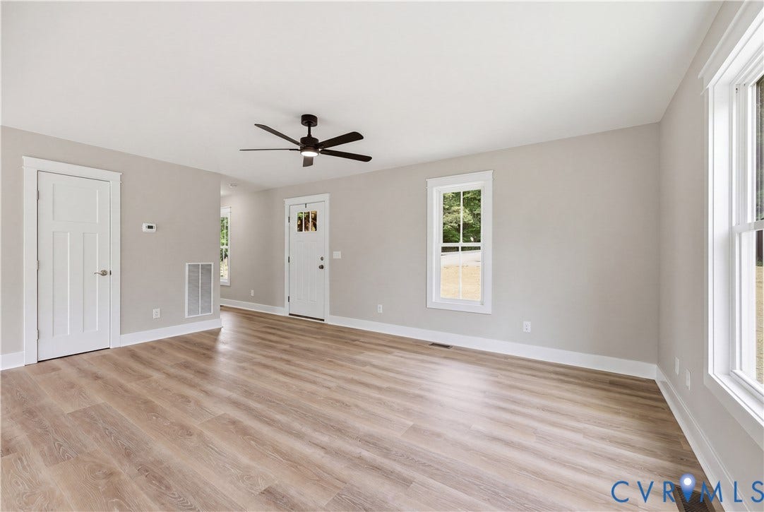 Spacious living area featuring wood-finish flooring, a contemporary ceiling fan, and light gray wall tones