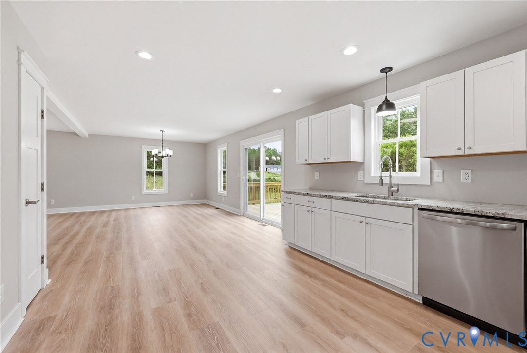 Open-concept kitchen and living area featuring wood-finish flooring, white cabinetry, granite countertops, and stainless steel appliances