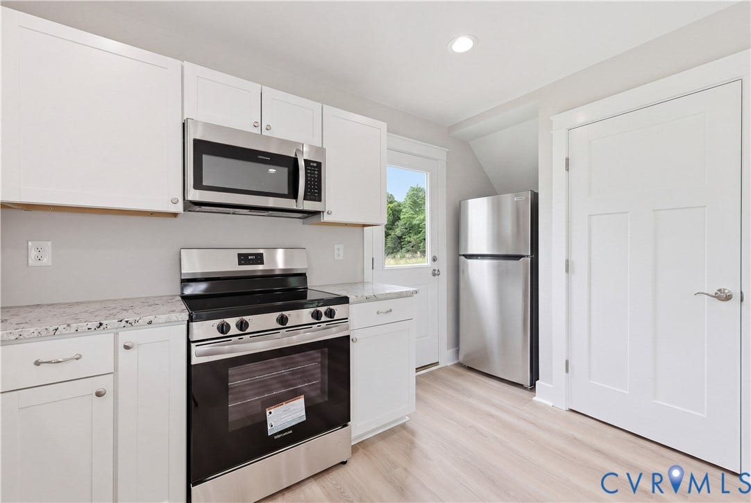Kitchen featuring white shaker cabinetry, speckled countertops, stainless steel appliances including a range and microwave, and light wood-finish flooring