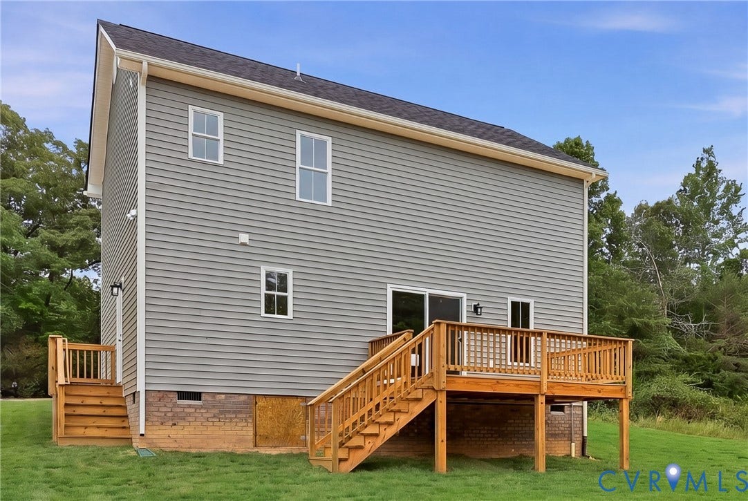 Rear exterior featuring a large wooden deck with railing, sliding glass door access, light gray horizontal siding, and white-framed windows