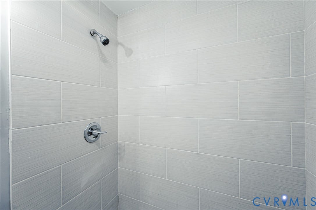 3903 Delmont Street, Henrico, VA 23222 Shower enclosure featuring light-toned rectangular wall tiles, a chrome showerhead, and a circular chrome handle with an integrated control lever
