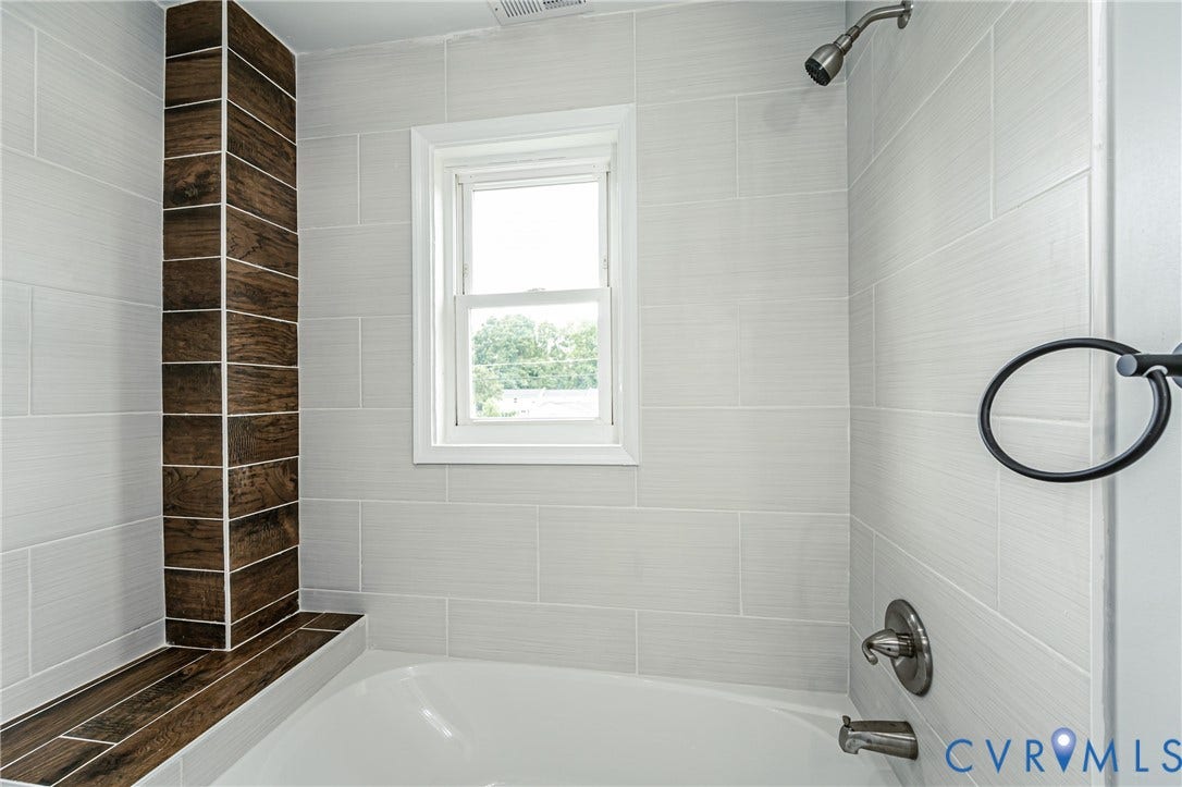 3903 Delmont Street, Henrico, VA 23222 Bathtub enclosure featuring light grey tile walls and a wood-finish tile accent column