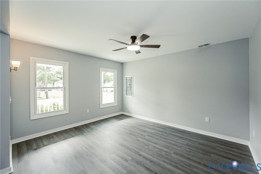 3903 Delmont Street, Henrico, VA 23222 Spacious room with light gray walls, wood-finish flooring, two large windows with white trim, and a contemporary ceiling fan with integrated lighting