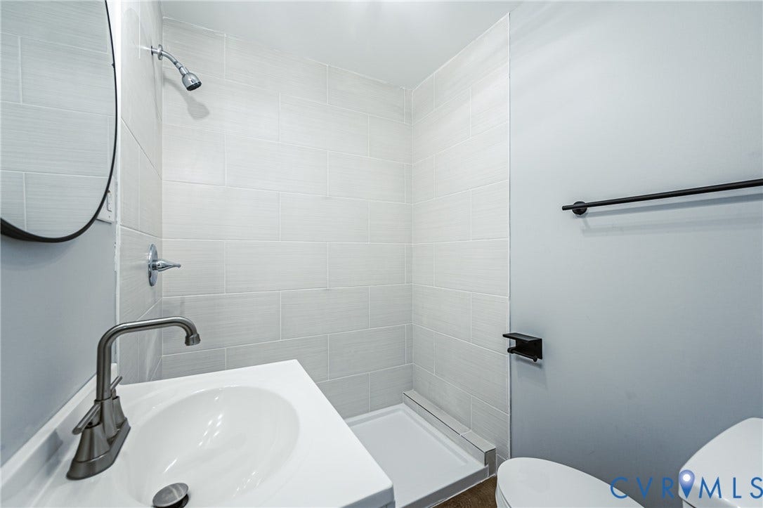3903 Delmont Street, Henrico, VA 23222 Bathroom featuring a tiled shower with a glass partition, a white vanity with an integrated sink, brushed nickel faucet, and a circular mirror