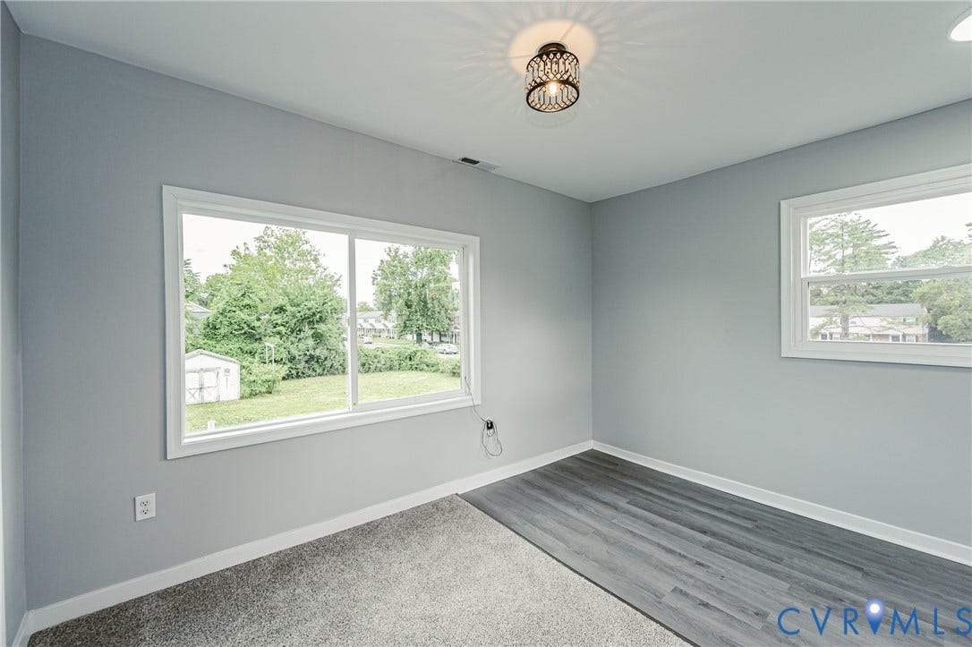 3903 Delmont Street, Henrico, VA 23222 Interior room featuring light gray walls, white trim, a decorative ceiling light fixture, two windows, wood-finish flooring, and gray carpeting