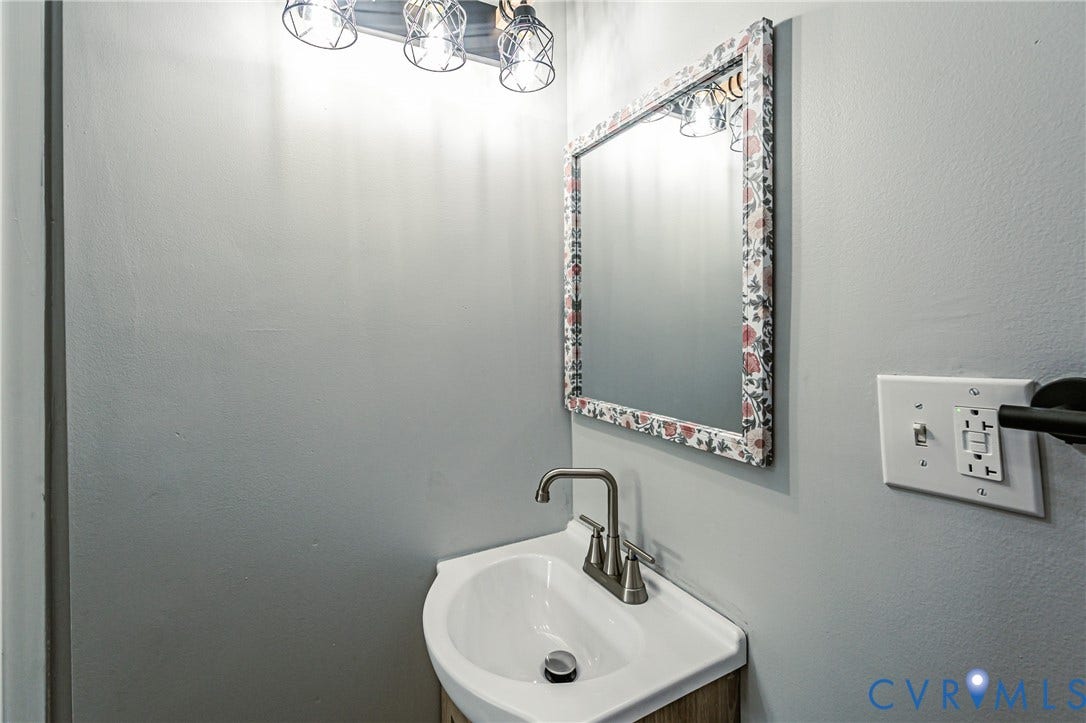3903 Delmont Street, Henrico, VA 23222 Wall-mounted corner sink with brushed nickel faucet, illuminated by a four-bulb vanity light fixture with cage shades