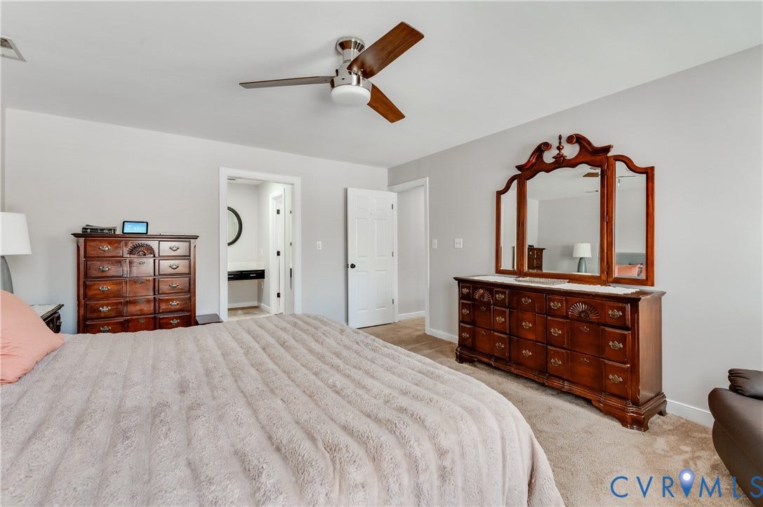 11611 Riverpark Way, Chesterfield, VA 23838 Interior room featuring neutral wall paint, carpet flooring, a ceiling fan with wood-finish blades, and a doorway opening to a bathroom with a circular mirror and floating vanity